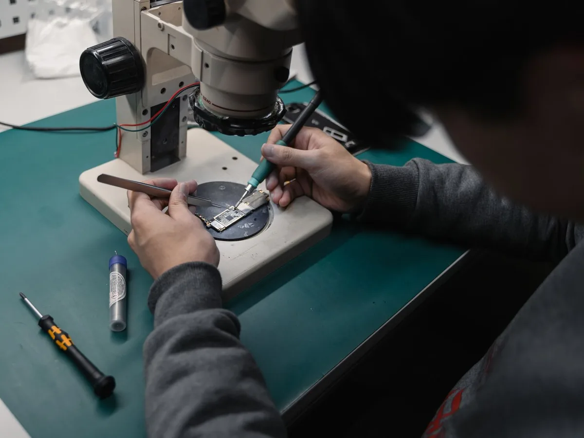 Certified repair technician performing board-level diagnostics under a professional microscope